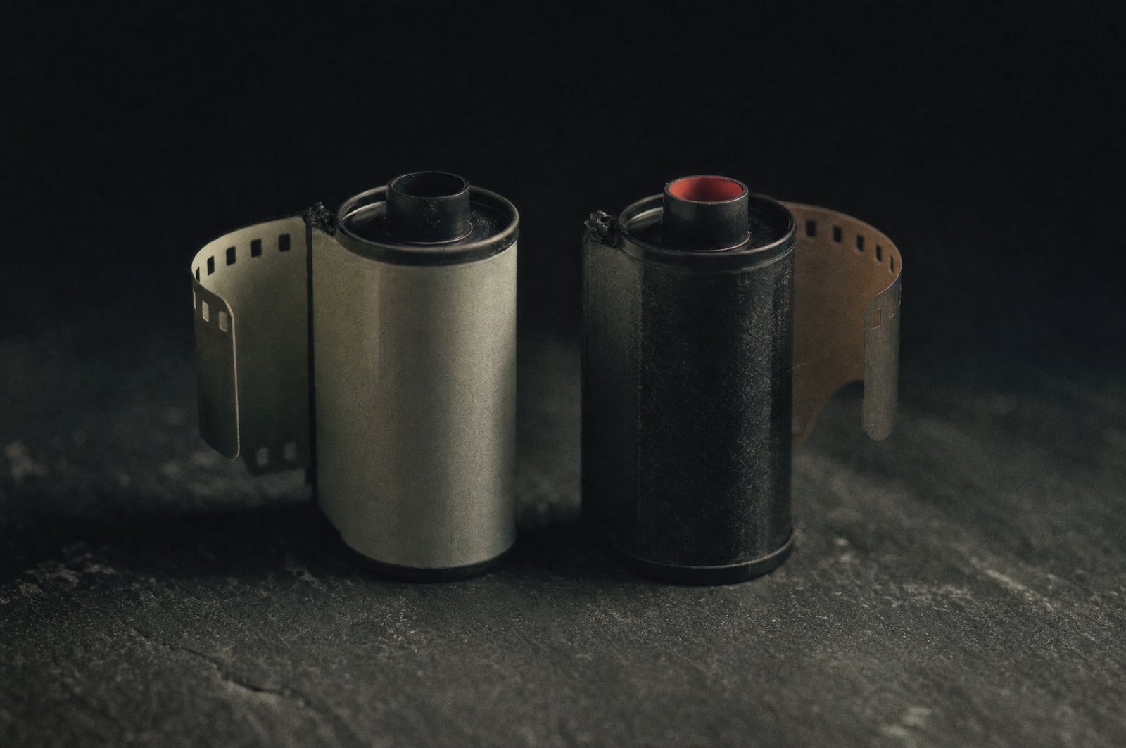 Two rolls of 35mm film standing face to face on dark slate